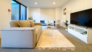 Ein modernes Wohnzimmer mit einer Couch, einem Couchtisch, einem Fernseher und einem Essbereich mit Stühlen und einem Tisch.