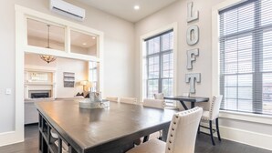 A spacious dining area with a large wooden table, white upholstered chairs, and a built-in shelving unit. - The Cullom-2BR Gem in the Heart of Town (Livingston)