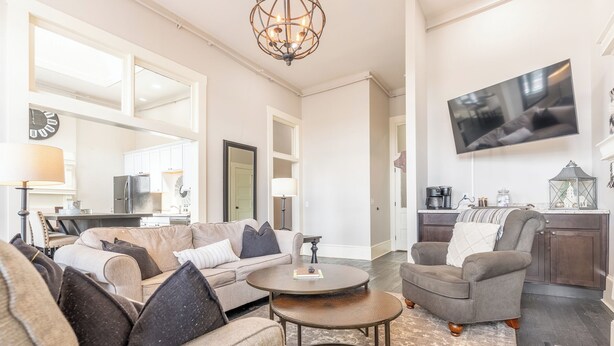A spacious living room with a large sofa, a coffee table, and a television mounted on the wall. - The Cullom-2BR Gem in the Heart of Town (Livingston)