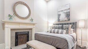 A bedroom with a fireplace, a bed with a tufted headboard, and a large mirror above the mantel. - The Cullom-2BR Gem in the Heart of Town (Livingston)