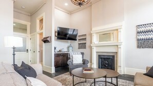 A living room with a sofa, armchair, coffee table, fireplace, TV, and artwork. - The Cullom-2BR Gem in the Heart of Town (Livingston)