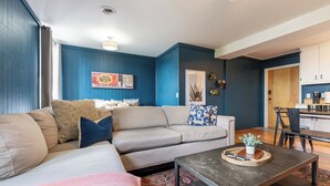 A living room with a beige sofa, a coffee table, and a rug. There is a dining area with a table and chairs. - The Mason Apartment-Cozy Getaway (Livingston)