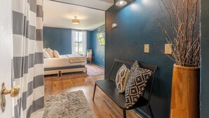 A bedroom with a bed, a bench with cushions, a rug, and a vase with branches. - The Mason Apartment-Cozy Getaway (Livingston)