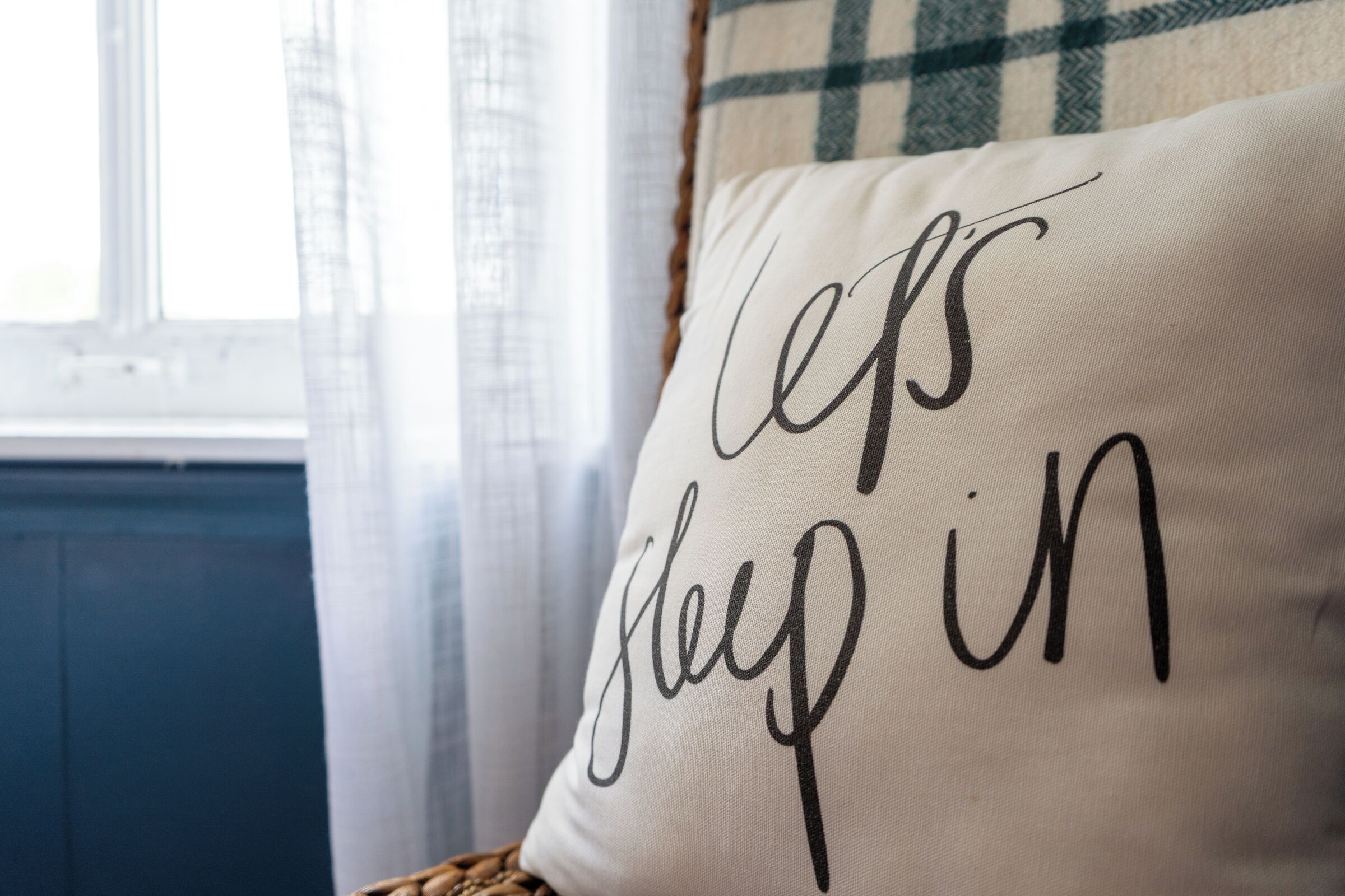 A pillow with the text "Let's sleep in" on a bed.