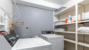 Un espace buanderie comprenant un lave-linge, un sèche-linge et des étagères où sont rangés les produits de nettoyage.