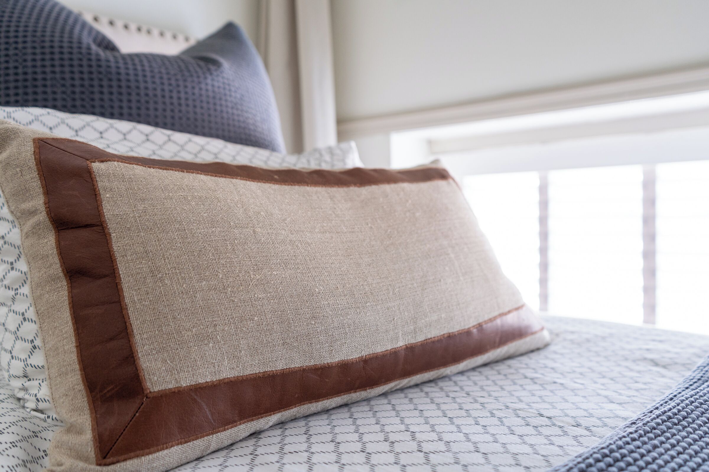 A bed with a patterned bedspread and a pillow with a brown leather edge.