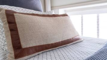 A bed with a patterned bedspread and a pillow with a brown leather edge.
