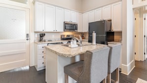 Una cocina moderna con armarios blancos, una isla central con taburetes de bar, un refrigerador de acero inoxidable y un microondas.