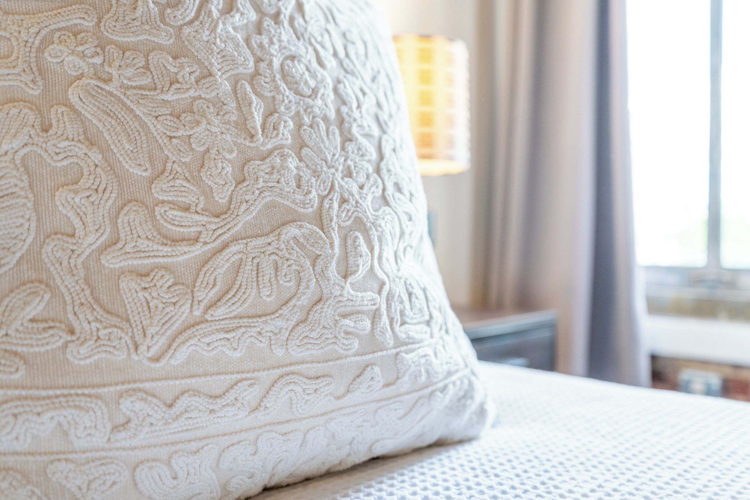 A close-up of a white, intricately embroidered pillow on a bed.