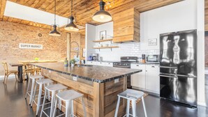 A modern kitchen with a central island, bar stools, stainless steel appliances, and a brick wall with a 'Supermarket' sign.