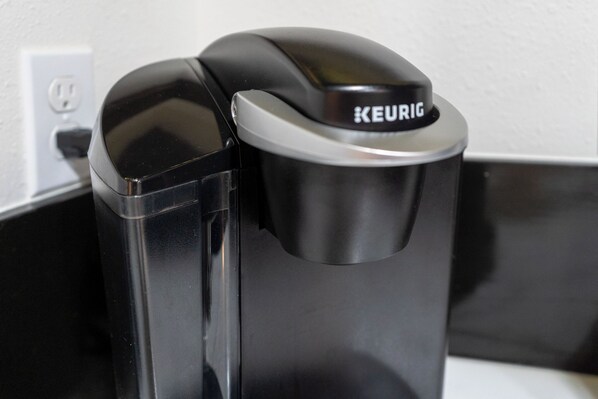 A black Keurig coffee machine with a silver base, positioned next to a white wall socket.