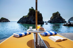 A sun lounger with a table set for breakfast, overlooking a calm sea with rocky outcrops. - Gardenia Mare Apartments | 1-Bedroom Ocean View & Panoramic Beach Suite (Ischia)