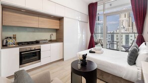 Een moderne hotelkamer met kitchenette, een bed, een klein rond tafeltje en uitzicht op de stad.