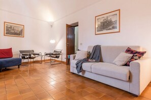 Ein Wohnzimmer mit einer Couch, einem Sessel, einem kleinen Tisch und zwei gerahmten Bildern an der Wand.