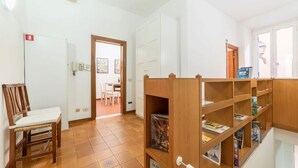 A room with a wooden chair, a bookshelf, a door leading to another room, and a tiled floor. - Casa dell'Arco - WelcometoRhome (Roma)