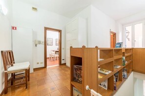 Ein Zimmer mit einem Holzsessel, einem Bücherregal, einer Tür zu einem anderen Raum und einem Fliesenboden.