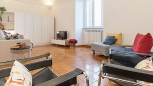 A living room with a sofa, a chair, a TV, a radiator, and a window. - Casa dell'Arco - WelcometoRhome (Roma)