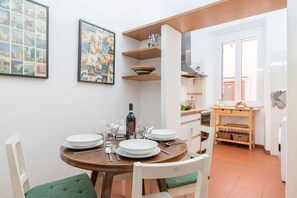 A dining area with a round table, chairs, and a bottle of wine. There are two framed pictures on the wall. - Casa dell'Arco - WelcometoRhome (Roma)