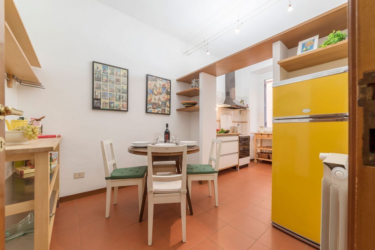 Cocina compacta con comedor, refrigerador amarillo y estante de pared con objetos.