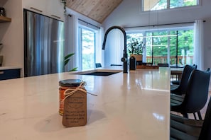 Eine Küche mit einer großen Kochinsel, einem Edelstahlkühlschrank und Blick ins Freie durch große Fenster.