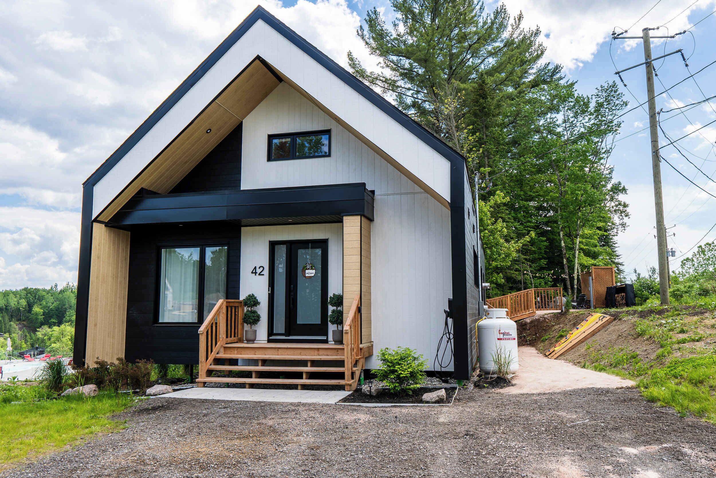 A modern two-story house with a black and white exterior, a wooden front porch, and a number '42' on the door.