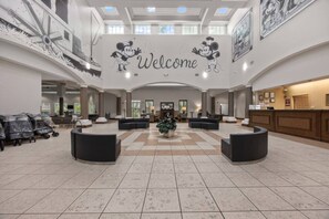Un'ampia hall con una reception centrale, diverse zone relax e un grande cartello con la scritta 'Welcome' raffigurante Topolino.
