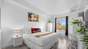A modern bedroom with a large bed, a desk, and a view of autumn trees. - 2 Bedroom Deluxe - Theme Park (Orlando)
