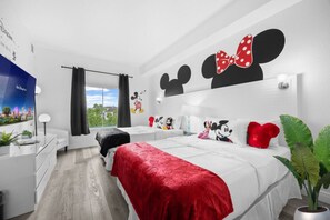 Una camera da letto moderna con un letto grande, un quadro a parete raffigurante Topolino e una TV che mostra un tema Disney.