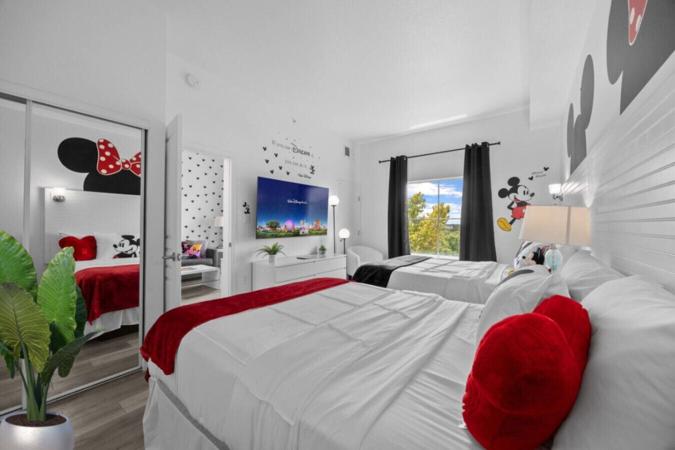 A hotel room with two beds, a TV, a window with curtains, and Mickey Mouse decorations.