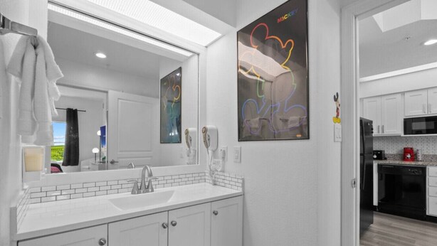 A modern bathroom with a large mirror, white cabinetry, and a view of the kitchen. - 2 Bedroom Deluxe - Theme Park (Orlando)