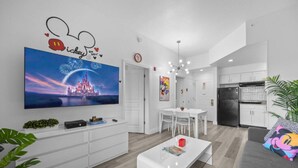 A modern living room with a flat-screen TV, white furniture, and a Mickey Mouse wall decal. - 2 Bedroom Deluxe - Theme Park (Orlando)