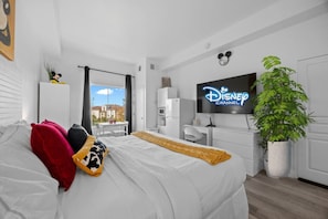 Una camera d'albergo con un letto, una TV che mostra 'Disney Channel', una pianta in vaso e vista sui palazzi.