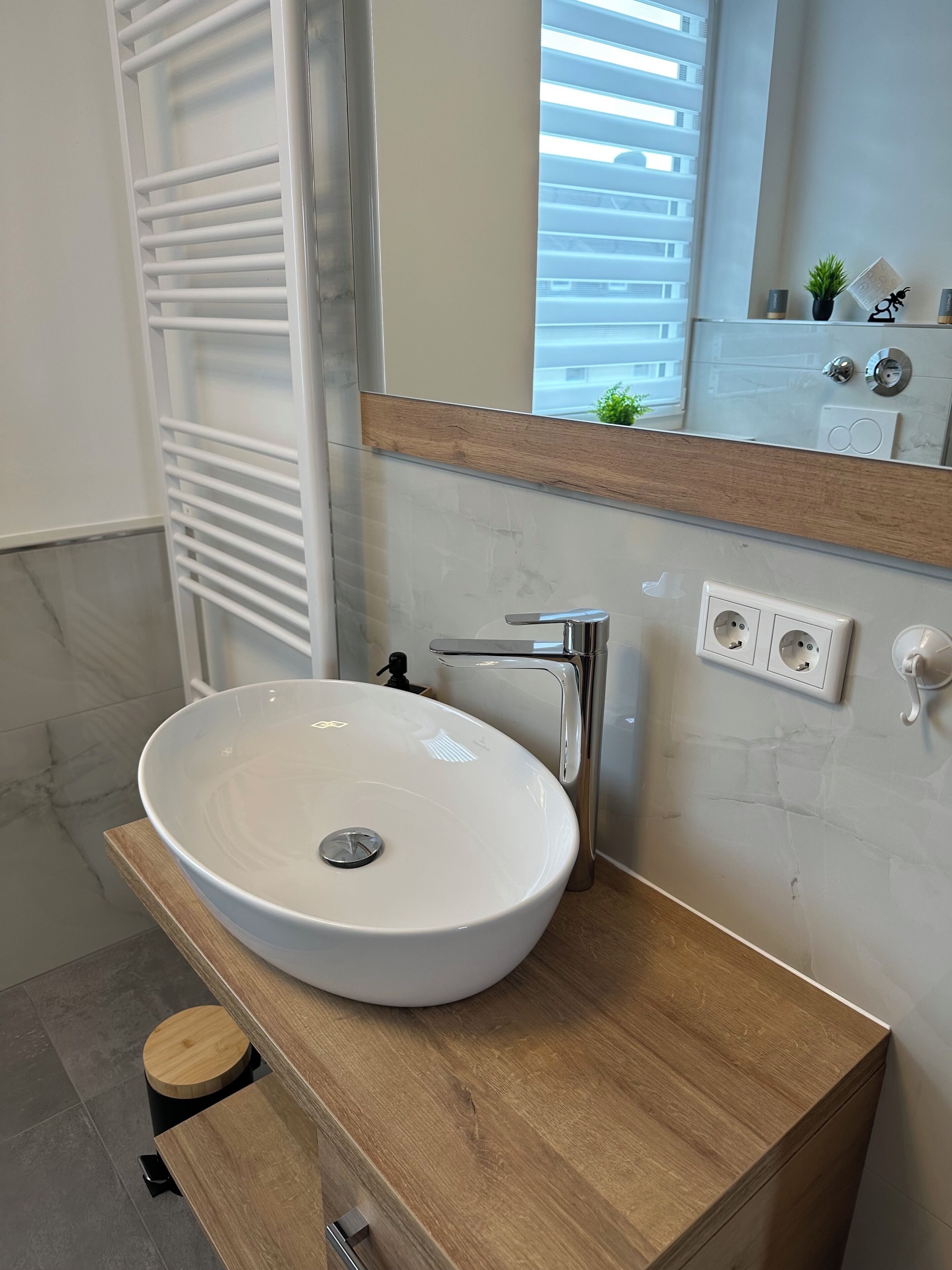 Ein modernes Badezimmer mit einem weißen Waschbecken, einer Holzausstattung und einem großen Spiegel.