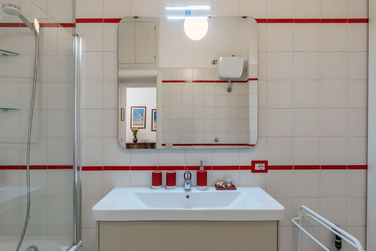 Une salle de bain avec une douche, un lavabo, un miroir et des murs recouverts de carreaux rouges.