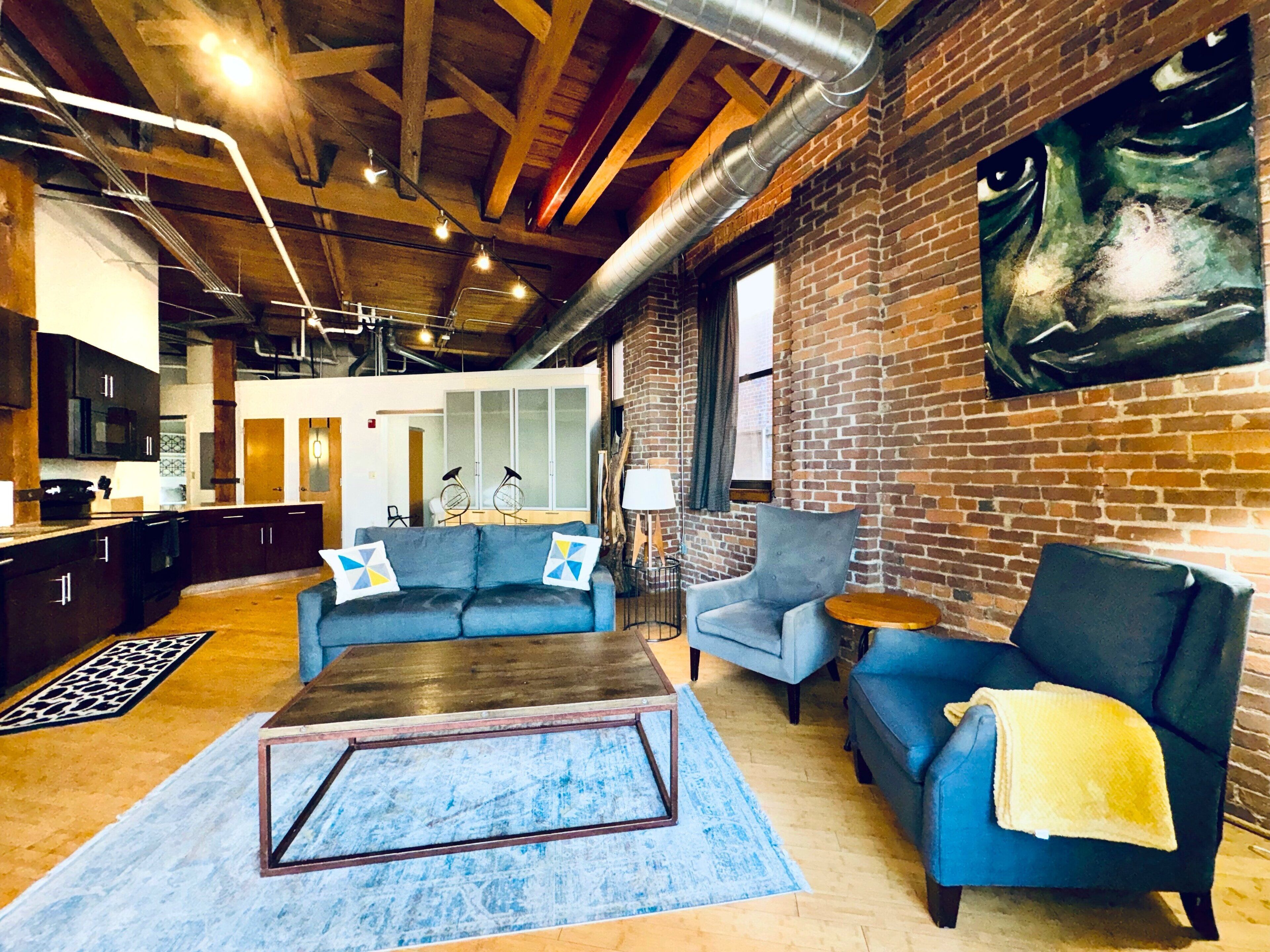 A spacious living area with a blue sofa, a coffee table, and a brick wall with a large painting.