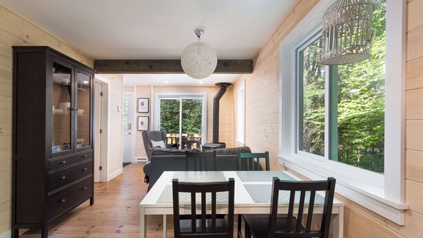 Un área de comedor con una mesa y sillas, un mueble de madera oscura y un ventanal con vistas a zonas verdes.