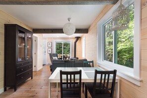 Ein Essbereich mit Tisch und Stühlen, einem dunklen Holzschrank und einem großen Fenster mit Blick ins Grüne.