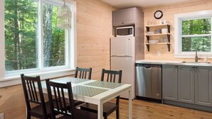 Una cocina moderna con paredes de madera, una mesa de comedor con sillas, microondas, refrigerador y lavavajillas.