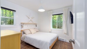 Un dormitorio con una cama de madera, una mesita de noche, un adorno con forma de estrella en la pared y dos ventanas con cortinas.