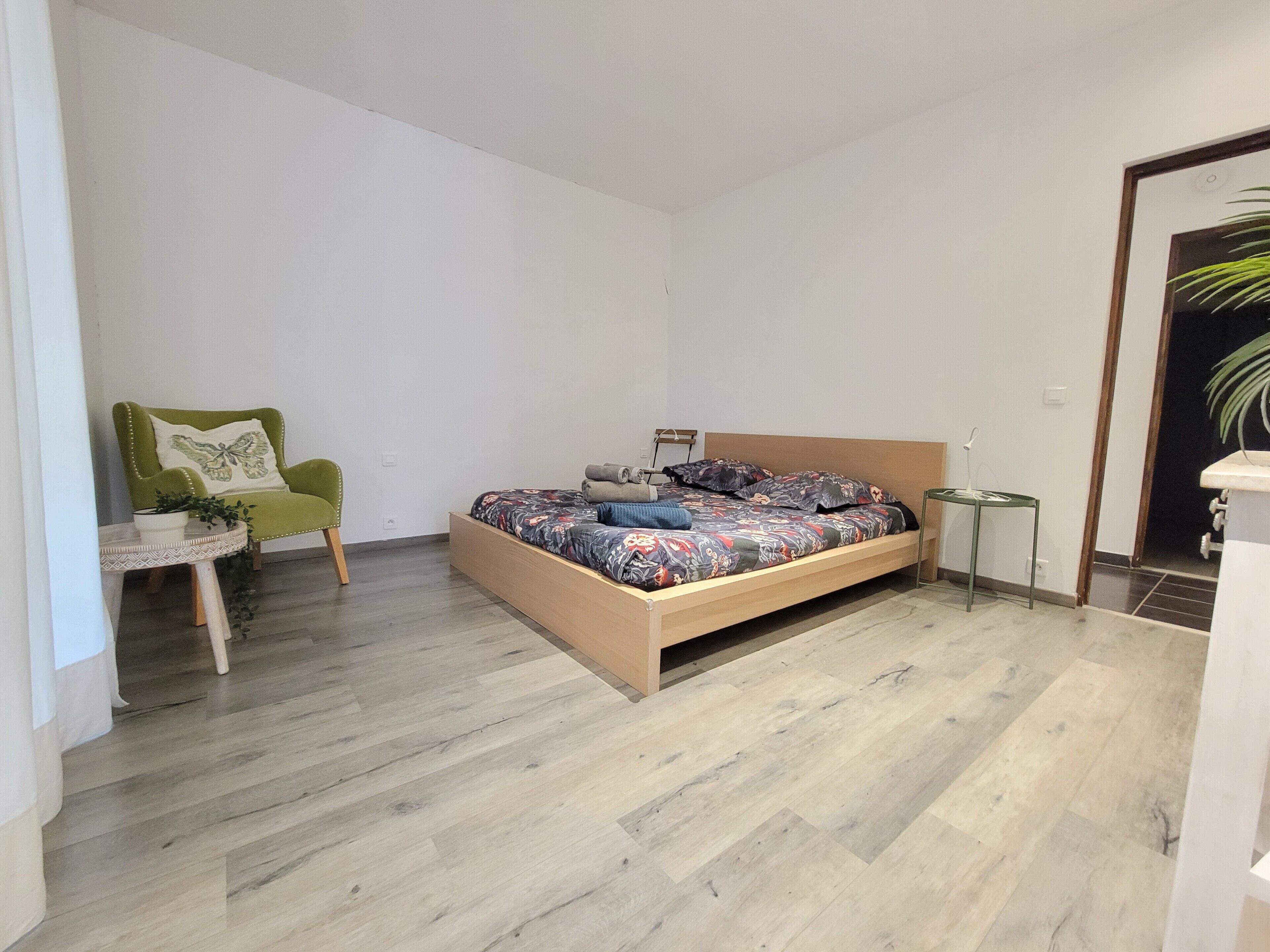 A bedroom with a bed, a chair, a small table, and a plant.