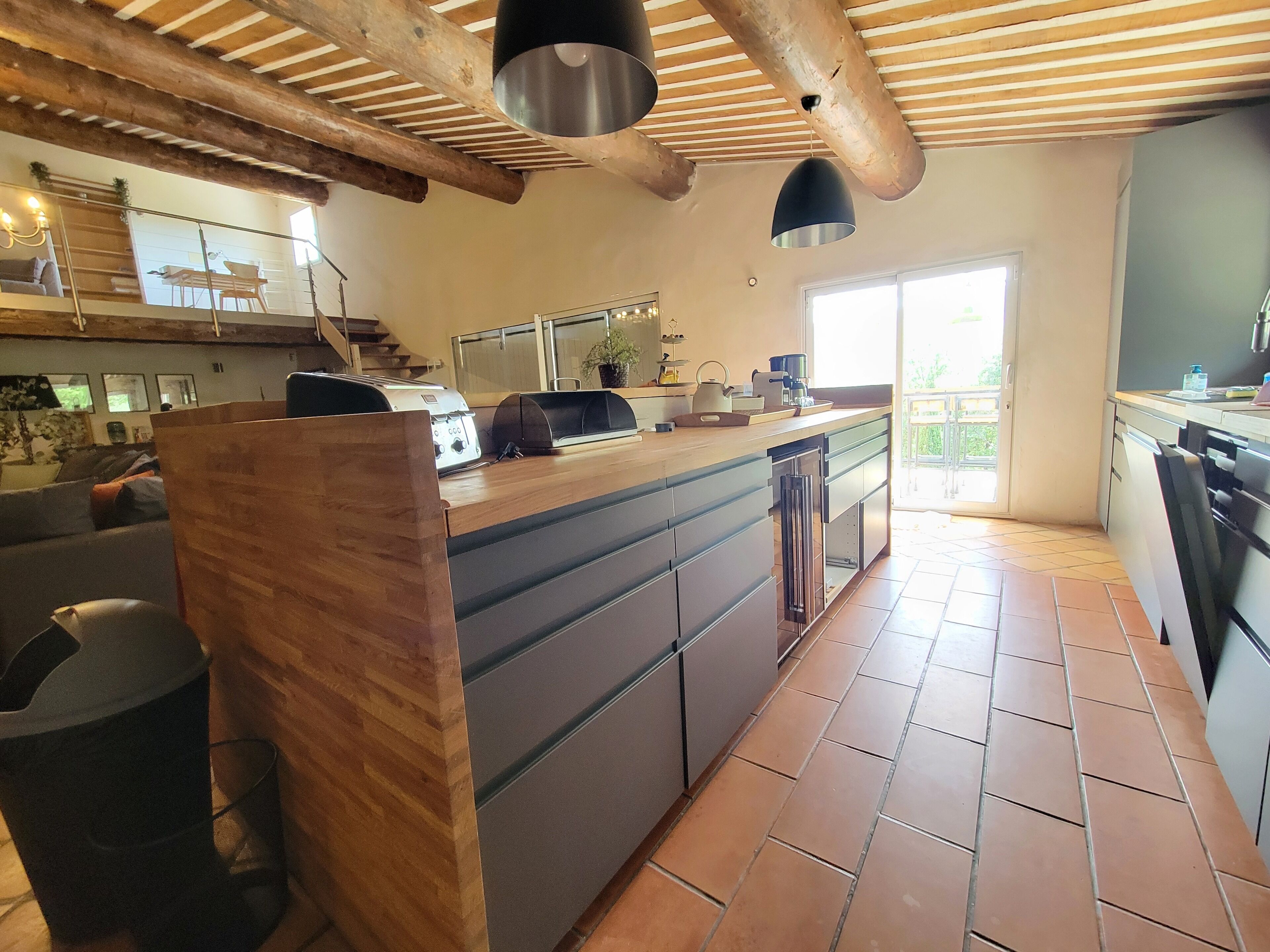 A spacious kitchen with a large island, wooden beams, and a sliding glass door leading to an outdoor area.