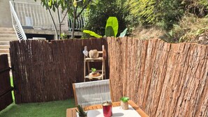 A wooden table with two chairs, a red container, and two potted plants in a backyard with artificial grass and a wooden fence. - Romantic room (Les Arcs)