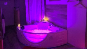 A room with a hot tub, wooden beams, a shower area, and a bed with patterned bedding. - Romantic room (Les Arcs)