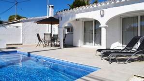 A swimming pool with lounge chairs and a table, surrounded by a white building with large windows and a tiled roof. - 05 Ch3200 in Denia With 3 Bedrooms and 2 Bathrooms (Denia)