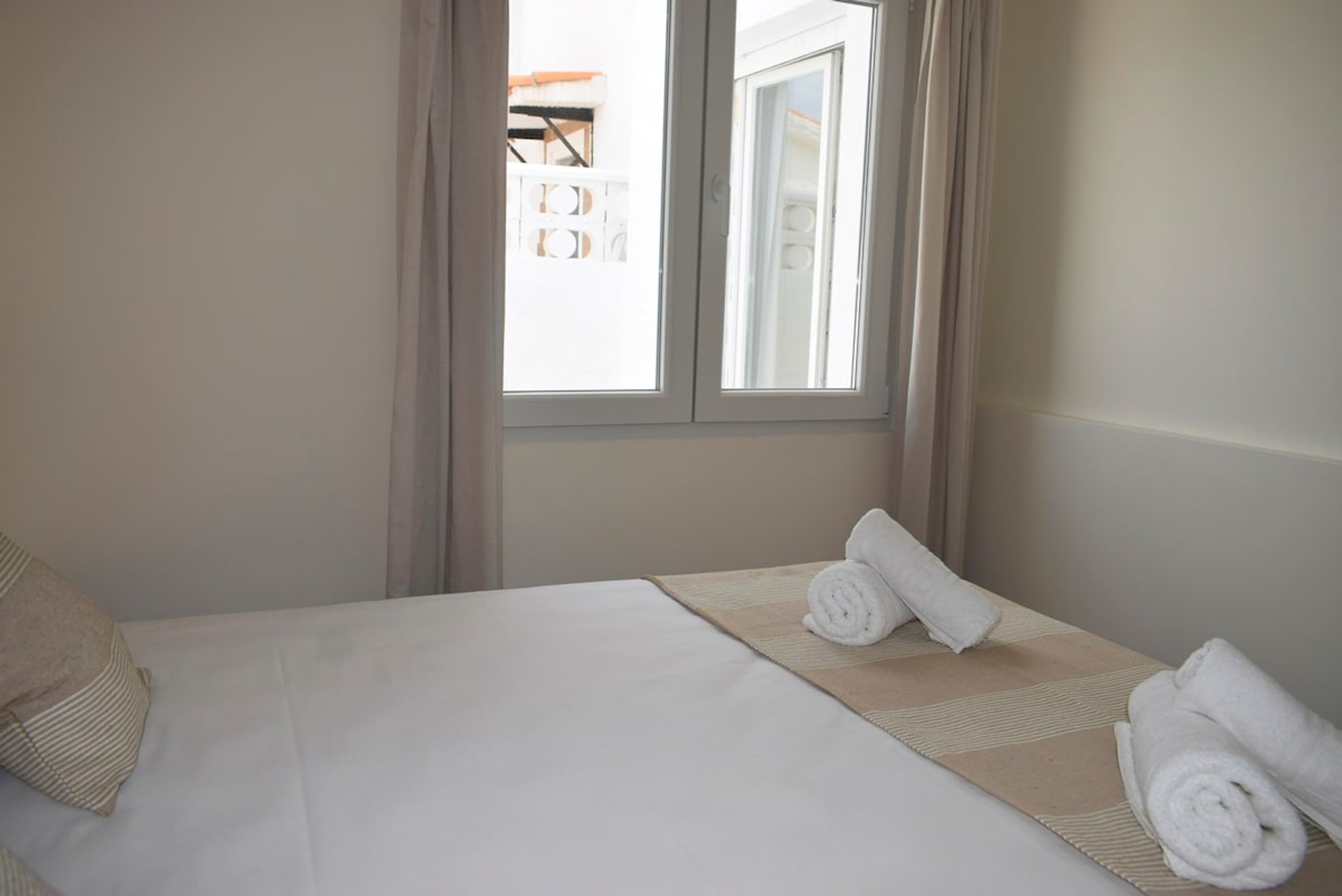 Une chambre d’hôtel avec un lit, deux serviettes enroulées, une fenêtre avec des rideaux et une vue sur le balcon extérieur.