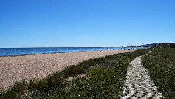 A beach with a wooden boardwalk leading to the shore, clear skies, and a few people in the distance. - 05 Ch3200 in Denia With 3 Bedrooms and 2 Bathrooms (Denia)