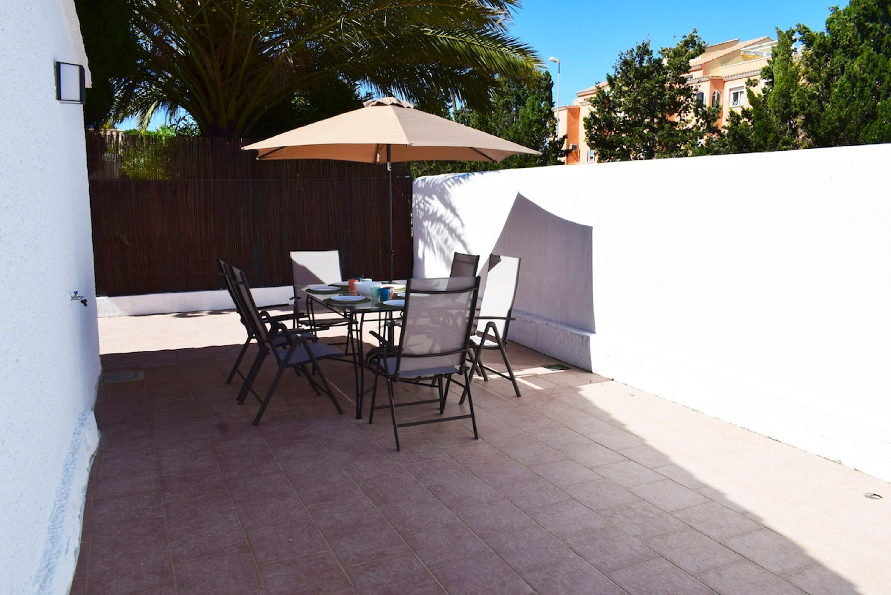 An outdoor patio with a table and chairs, a large umbrella, and a wooden fence.