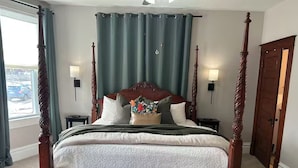 Ein Bett mit Himmelbett, einem gepolsterten Kopfteil, einer dekorativen Kissenanordnung und einem Nachttisch mit Lampe.