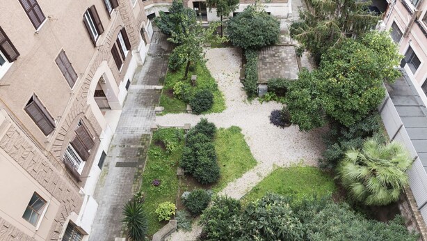 Ein Innenhof mit einem zentralen Garten, umgeben von Gebäuden mit zahlreichen Fenstern und Balkonen.