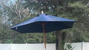 An outdoor patio area with a table and chairs, a blue umbrella, and a white fence in the background. - Orlando Getaway 3/2 Close to Theme Parks (Orlando)